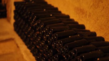 Loş aydınlatılmış mahzende saklanmış şarap şişeleri.