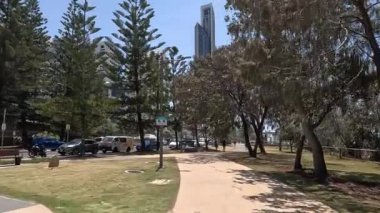 İnsanlar binaların yakınındaki güneşli bir şehir parkında yürüyor