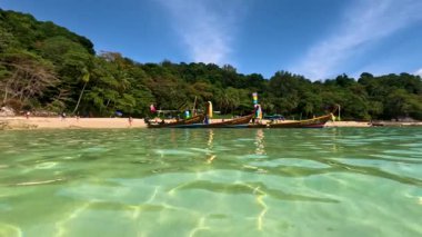 Uzun kuyruklu botlar, Phuket, Tayland 'da güpegündüz yemyeşil, tropik bir plajın yakınında turkuaz sularda yüzerler.