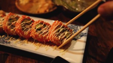 Yemek çubukları dekoratif bir tabaktan suşi topluyor.