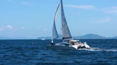 Açık mavi gökyüzü ve parlak güneş ışığı altında Ko Racha Yai, Phuket yakınlarında bir yelkenli süzülüyor.