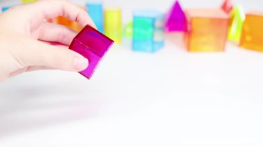 Eller, beyaz bir tablo üzerinde canlı üç boyutlu geometrik şekilleri manipüle ederek, çeşitli şekilleri ve renkleri parlak ışıklandırmada gösterir