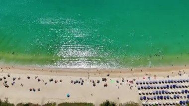 Drone footage captures vibrant umbrellas and swimmers at Nai Harn Beach, Phuket, under bright sunlight with turquoise waters