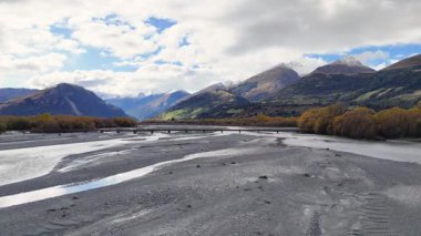 Dağları ve sonbahar yapraklarıyla dolu huzurlu bir nehir yatağı parçalı bulutlu bir gökyüzünün altında, doğal gün ışığında ele geçirilmiş.