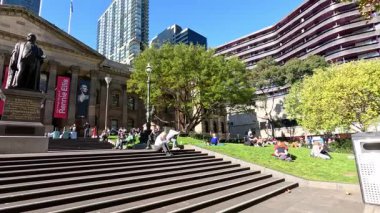 İnsanlar kütüphanenin dışında güneşli bir günün tadını çıkarıyor.