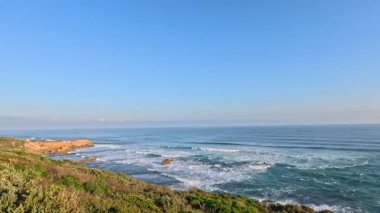 Dalgalar açık gökyüzünün altında kayalık kıyılara çarpıyor.