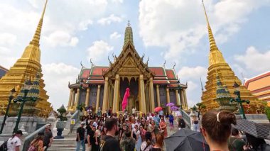 Kalabalık Bangkok 'ta Wat Phra Kaew' i keşfediyor, parlak gün ışığında canlı bir mimariyi yakalıyor. Sahne canlı ve hareketli.