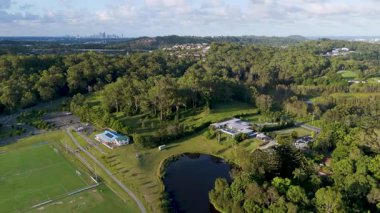 İnsansız hava aracı görüntülerinde yemyeşil ve berrak gökyüzünün altında dingin bir gölet bulunan bir spor kompleksi görülüyor.