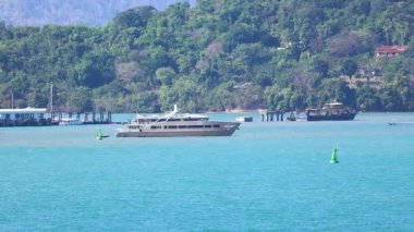 Lüks bir yat Phuket 'in turkuaz denizinde süzülüyor. Parlak gün ışığında yemyeşil tepelere doğru batıyor.