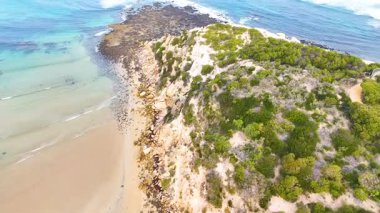 Beyaz kumsalda kayalar ve dalgaların olduğu güzel deniz manzarası.