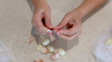 Açık mutfak tezgahında sarımsak karanfili soyan ellerin yakın çekimi. Doğal ışıklandırma, sabit kamera, mutfak hazırlıklarına odaklanmış.