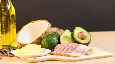 Yumuşak ışıklandırmalı ahşap bir yüzeye yerleştirilmiş yağlar, avokadolar ve fındıklar dahil olmak üzere çeşitli sağlıklı yağlar.