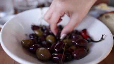 Bir el, normal bir yemek atmosferi yaratmak için ahşap bir masanın üzerindeki bir kaseden marine edilmiş zeytinleri topluyor.