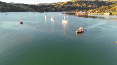 İnsansız hava aracı, sakin sular ve manzaralı tepeler eşliğinde Yeni Zelanda 'nın Akaroa kentindeki sakin tekne ve manzaraları yakalar.