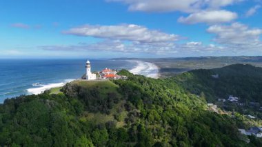 Berrak gökyüzünün altında yemyeşil ve okyanus manzaralı Byron Körfezi deniz fenerinin hava görüntüleri.