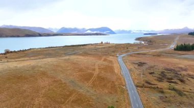 Hava görüntüleri Tekapo Gölü 'nün yanında sakin bir yol yakalar ve yumuşak, doğal ışıklandırma altında geniş manzaralar sergiler.