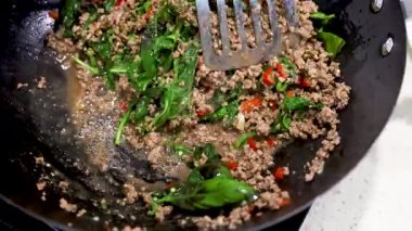 Parlak ışık altında canlı malzemelerle bir tavada biftek ve fesleğen kızartması pişirmek.