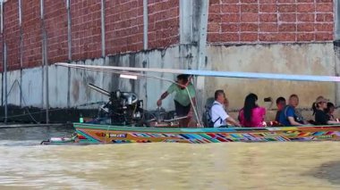Yolcularla dolu canlı bir tekne Bangkok, Tayland 'da bir kanal boyunca seyahat ediyor. Sahne şehir yaşamını ve su yolu aktivitesini yakalıyor.