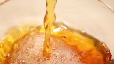 Altın çayın bir bardağa doldurulup sıcak ışık altında kabarcıklar ve köpükler oluşturulduğu yakın plan.