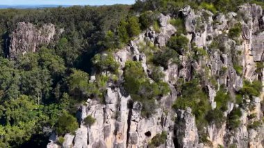 Drone footage captures the rugged Nimbin Rocks surrounded by lush greenery under bright daylight