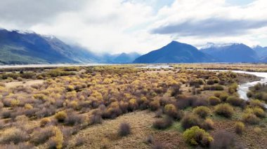 Aerial view of Glenorchy's vast landscape with mountains, vibrant foliage, and a winding river under cloudy skies