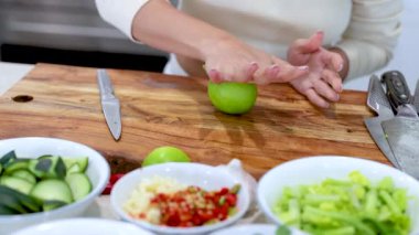 A person rolls a lime on a wooden cutting board in a bright kitchen setting