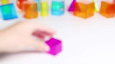 A hand manipulates vibrant 3D geometric shapes on a white surface, highlighting educational and playful interaction