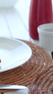 A spoon drizzles ketchup onto fried chicken on a white plate, set on a woven mat in bright lighting