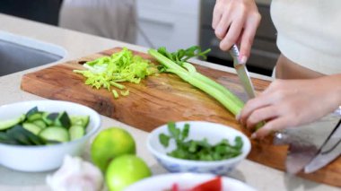 Hands slicing celery on a wooden board in a bright kitchen. Fresh ingredients and natural lighting create a clean, inviting atmosphere