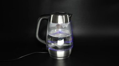 Kadın elleri siyah arka planda elektrikli su ısıtıcısını kapatıyor.