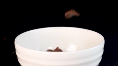 Chocolate cereal flakes cascade into a white bowl against a black backdrop, creating a dynamic and appetizing visual