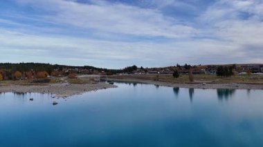 Drone footage captures Lake Tekapo's serene waters and surrounding landscape under a clear sky, showcasing natural beauty and tranquility