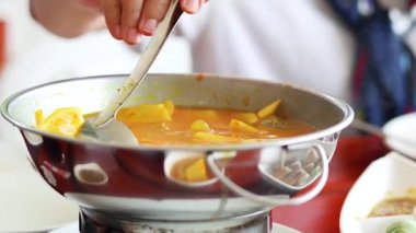 Metal tencerede sarı köri karıştıran kişi