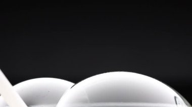 A wand interacts with soap bubbles, creating reflections and colors against a dark background in a minimalist setting