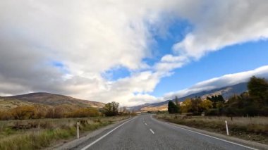A serene drive through Wanaka, New Zealand, showcasing expansive skies, lush greenery, and distant mountains under dynamic lighting