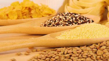 Various grains and pasta displayed with warm lighting, highlighting textures and colors. Includes quinoa, lentils, tagliatelle, and corn