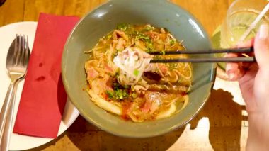 Chopsticks lift noodles from a flavorful Vietnamese dish in a Bangkok restaurant, highlighting vibrant colors and inviting ambiance