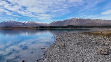 İnsansız hava aracı görüntüleri Tekapo Gölü 'nün sakin manzarasını yansıtıcı suları ve canlı bir gökyüzünün altındaki uzak dağları görüntüler.