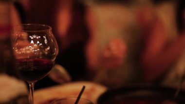 Şarap ve bulanık figürlerle samimi yemek sahnesi, sıcak aydınlatma, samimi bir atmosfer yakalama.