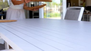 Bir insan, açık havada beyaz bir masanın üzerine dokuma kaplamalar yerleştiriyor ve hoş bir ortam yaratıyor.