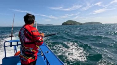 Tayland, Phuket 'te bir tekneden balık avlıyor. Parlak gün ışığı, berrak gökyüzü ve okyanus dalgaları dingin bir atmosfer yaratır.