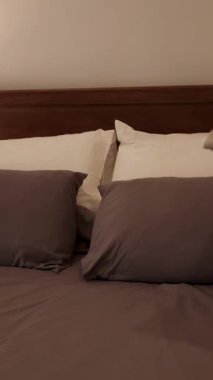 Eller, kareli yastıkları yumuşak ışıklı yatak odasındaki düzgün yapılmış bir yatağa yerleştirir ve sıcak ve davetkar bir atmosfer yaratır.