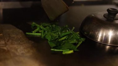 Chef stir-frying spinach and oysters in a wok