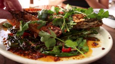 A vibrant dish of grilled mantis shrimp garnished with fresh herbs and spices, captured in a lively restaurant setting