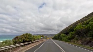 30 saniyelik bir video, Büyük Okyanus Yolu boyunca bir sürüş yakalıyor, kıyı manzarası, yemyeşil ve bulutlu gökyüzünün altında dolambaçlı yollar.