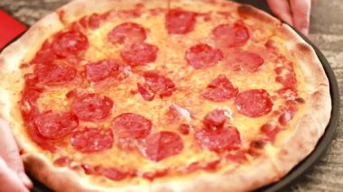 Eller taze pişmiş pepperonili pizzayı dilimliyor.
