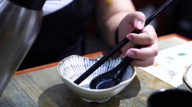 İnsan yemek çubuklarıyla bir kaseye su döker.