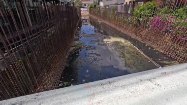 Kentsel ortamdaki bir kanal, parlak gün ışığında görünür kirlilik ve kimyasal atıkları göstererek, çevresel kaygıları vurguluyor