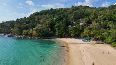 Turkuaz suları, yemyeşil yeşilliği ve dağınık turistleriyle sakin bir Phuket plajının havadan görünüşü. Güpegündüz yakalandılar.