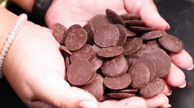 Eller nazikçe çikolata disklerini avuç içlerine koyuyor.